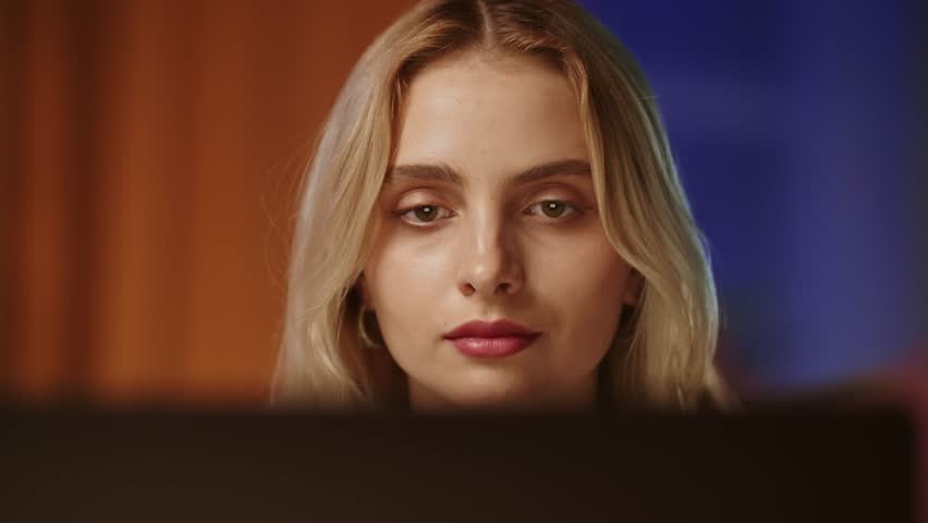 A young pretty blonde girl with a confident and arrogant gaze looks at the screen of a computer monitor or laptop. A pretty business lady corresponds and reads messages impartially with emotional | Shutterstock HD Video #1111832811