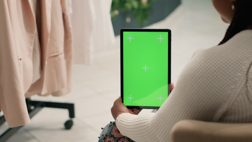Shopper in second hand clothing shop holding green screen tablet, trying to decide what clothes to purchase. Client looking at new collection of garments in discount store using chroma key device | Shutterstock HD Video #1111833083