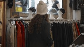 Young woman looking at clothes and accessories in second hand chic vintage store. Female going through stylish wear in hip concept store. 80s and 90s designed fashion on sale or clearance