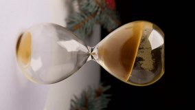 Christmas countdown hourglass, measuring the until the festive season. A clear hourglass filled with glimmering golden sand. the essence of Christmas spirit, magic, and dreams. Vertical video 