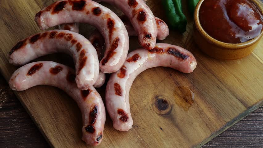 Natural sausages grill lay down on a cutting board with vegetables and red sauce. Slow motion.