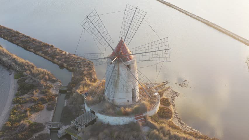 Windmill at sunset, Riserva Naturale Isole dello Stagnone di Marsala, salt flats in the evoporation pond, Trapani province, Sicily, Italy, Europe. Aerial view