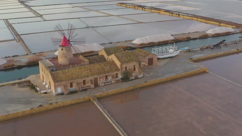 Windmill at sunset, Riserva Naturale Isole dello Stagnone di Marsala, salt flats in the evoporation pond, Trapani province, Sicily, Italy, Europe. Aerial view