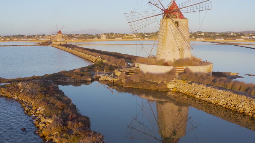 Windmill at sunset, Riserva Naturale Isole dello Stagnone di Marsala, salt flats in the evoporation pond, Trapani province, Sicily, Italy, Europe. Aerial view