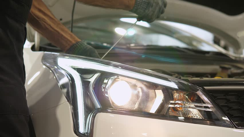 A close-up of a worker checks and adjusts the headlights of a car's lighting system at a service station with a screwdriver. Adjusting the brightness and tilt angles of the front headlights. Royalty-Free Stock Footage #1111843223