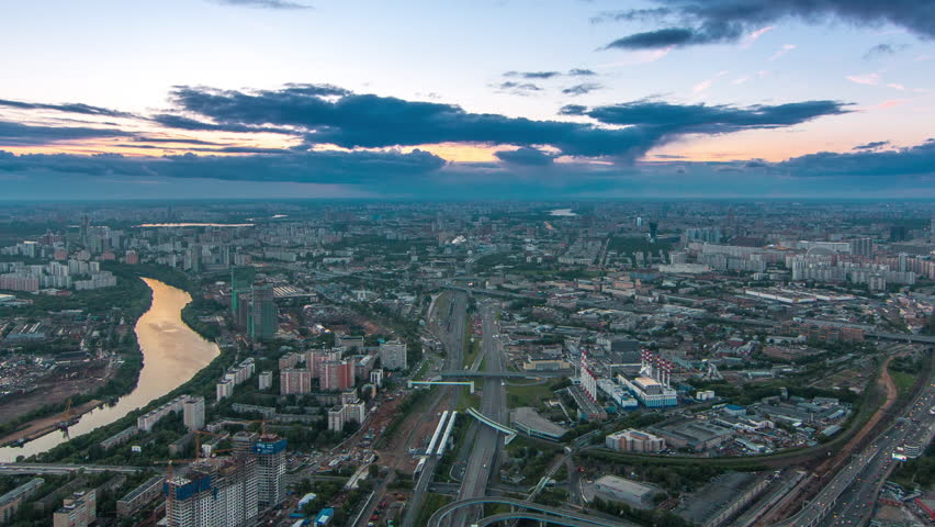 Aerial top view of Moscow city day to night transition timelapse after sunset. From the observation platform of the business center of Moscow City. Moscow river and traffic on roads at summer evening