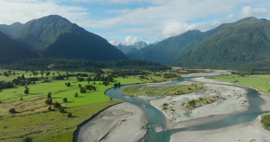 Rising aerial view of idyllic, wild and rugged landscape with winding river and Southern Alps mountains on the West Coast of South Island, New Zealand Aotearoa