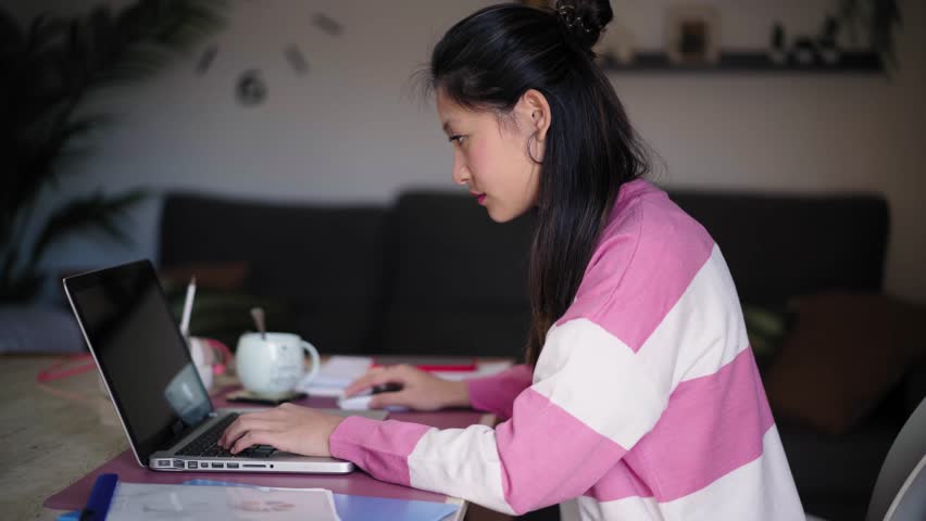 Side view of beautiful young Asian woman turning and posing cheerful looking at camera. Nice Chinese girl working concentrated from home in front of laptop. Empowered female gen z people, online job | Shutterstock HD Video #1111850563