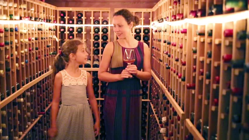 Pretty girl and her mother stand among shelves with wine in home cellar
