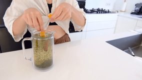 woman makes herbal tea in her kitchen. She adds leaves of mint, lemon balm, thyme, and rosemary to teapot . woman enjoys delicious and aromatic beverage.