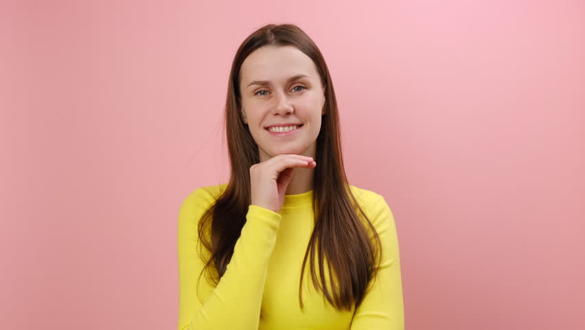 Portrait of positive attractive young caucasian woman looking at camera, flirting expression, expressing happy emotions, wearing yellow sweater, posing isolated on pink color background wall in studio | Shutterstock HD Video #1111861917
