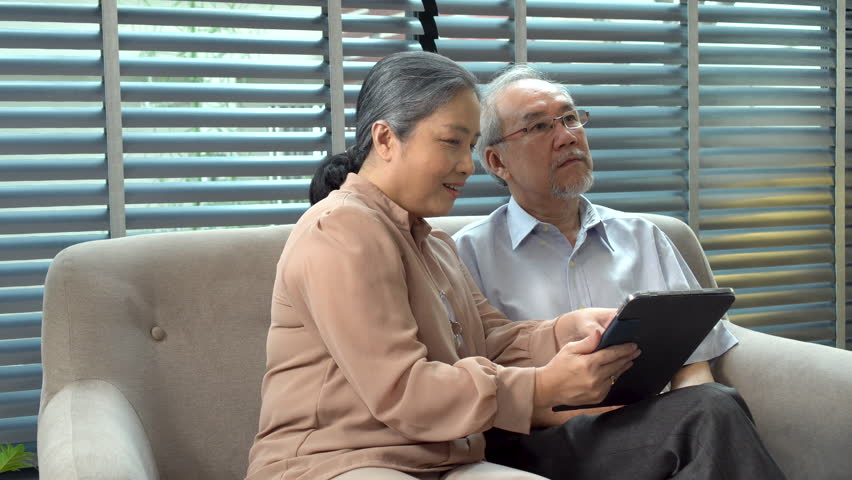 Grandmother pointing finger touchscreen picture on digital tablet for husband Alzheimer’s pain sitting together sofa at home.Elderly couple  memory disability patient health support care. Family care Royalty-Free Stock Footage #1111862031