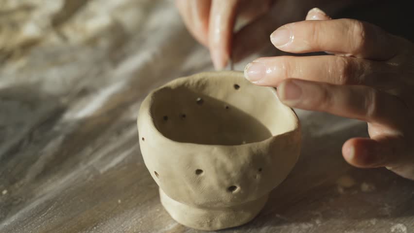 A woman makes holes using a tool in a clay craft - a candlestick. Close-up. Hobbies and creativity.