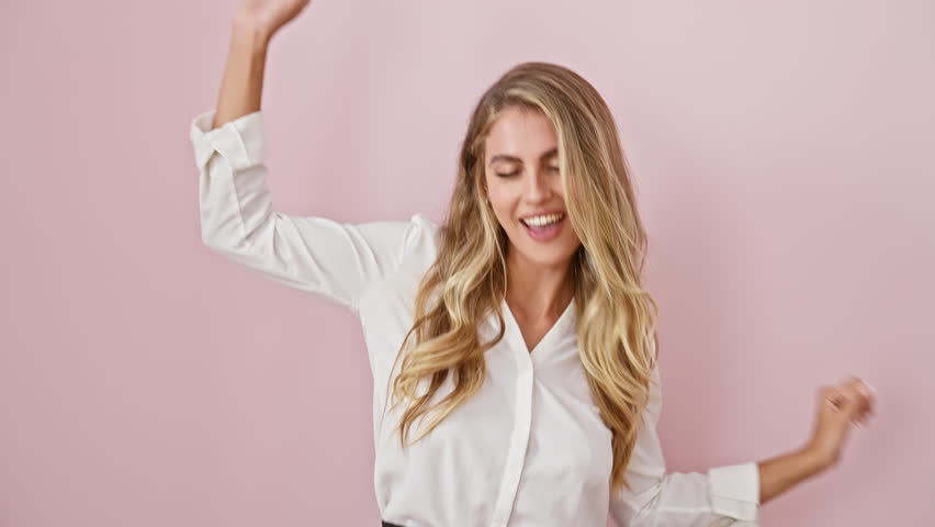 Overjoyed young blonde woman in casual shirt, confidently dancing to music, full of joy and cheerfulness, standing isolated over pink background, beaming with charming smile | Shutterstock HD Video #1111866255