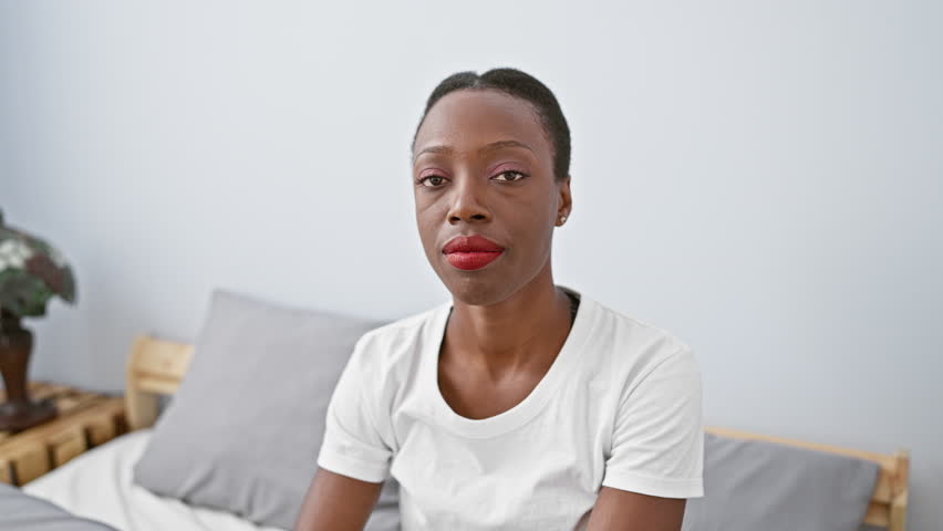 Depressed african american woman pointing downwards, lying in a bedroom, a portrait of an unhappy female, expressing sadness.
