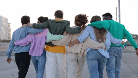 Rear view of young united group of multiracial friends walking together while hugging each other outside. Unity, youth community and international friendship concept.  Adlı Stok Video