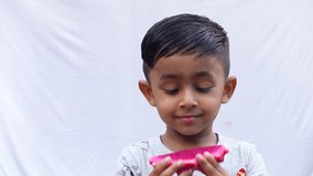 An Asian child is eating a slice of pink Dragon fruit on an isolated white background. Fresh fruit-eating and enjoying concept 4k video.