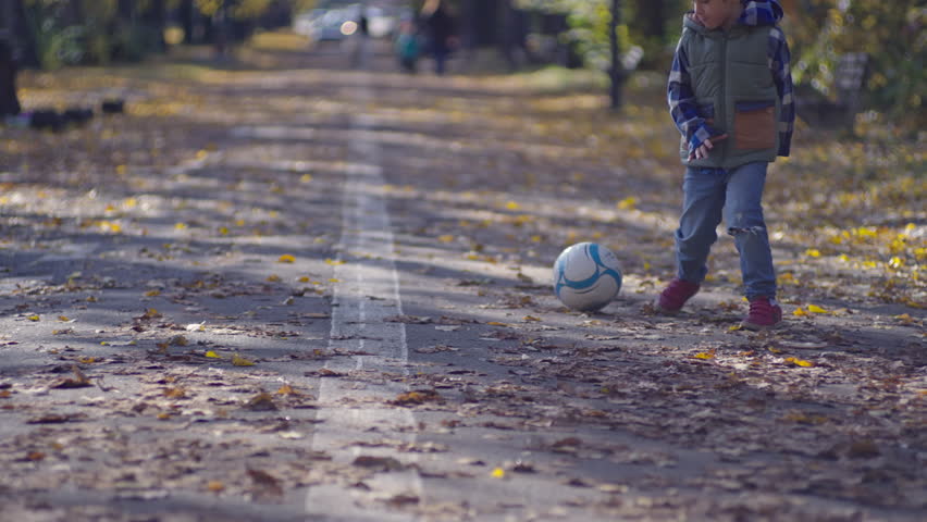 The boy plays football in the yellow leaves in the autumn park. The child kicks the ball, has fun and actively plays and rests. High quality 4k footage | Shutterstock HD Video #1111868463