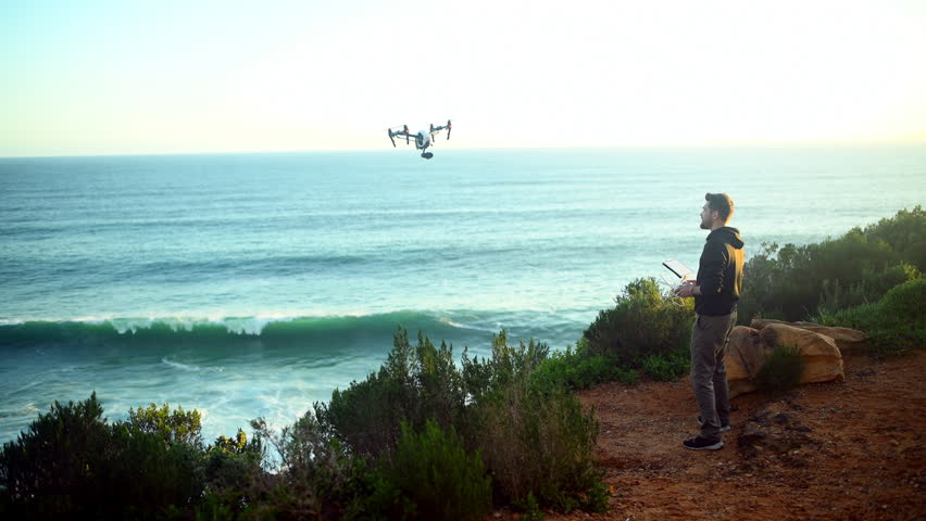 Drone, technology and man with photography on beach filming nature, water or landscape. Videography, photographer and test remote control in flight for aerial recording of ocean at sunset or sunrise | Shutterstock HD Video #1111874971