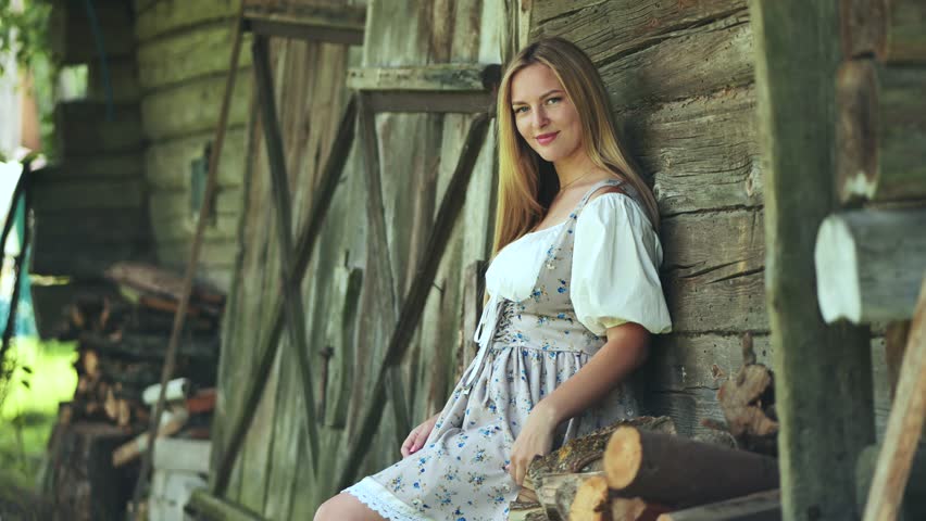 A girl of Slavic appearance poses in the countryside by the barn.