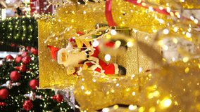 Vertical video of toy santa claus in red suit sits on armchair illuminated by yellow lights in shopping mall Cinematic video festive santa claus with holiday lights garlands waits for kids Santa claus