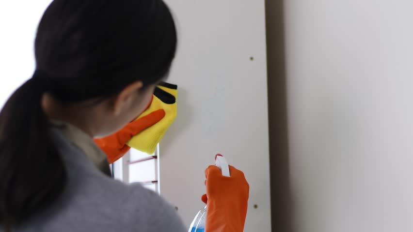 A house cleaning woman is spraying liquid and using a cloth to wipe down a cabinet in the house. | Shutterstock HD Video #1111877333