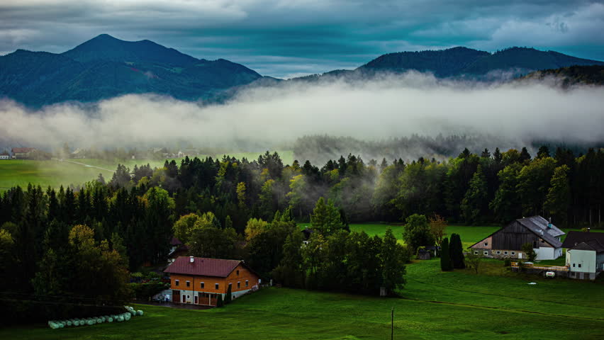 Cloudscape over a farm in Austria with low-lying fog in the valley - time lapse