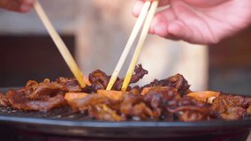 Close up of hand using chopstick cooking Japanese and korean BBQ Grill food. Cooking sliced meat on the grill pan using chopstick. Side view