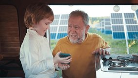 Grandfather and grandson relaxing in the kitchen of a camper van, talking and laughing against the backdrop of a field of solar panels - Powered by Shutterstock - Get 15% off with code: PIKWIZARD15