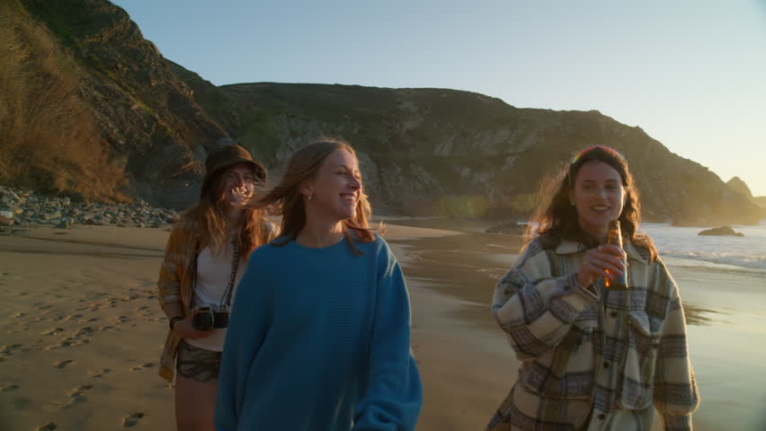 Three hipster millennial female friends walk on beach, sip on beer, make photos, laugh, smile and hang out. Summer outdoors new generation lifestyle | Shutterstock HD Video #1111887021