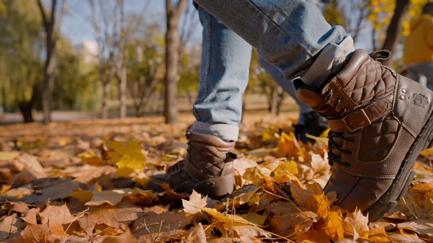 People in boots prefer spend time kicking fallen yellow leaves on lawn. Couple in jeans has walk together in city park in sunny weather slow motion | Shutterstock HD Video #1111890119