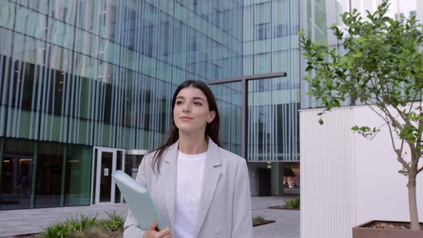 Cheerful young adult business woman walking outdoors corporate office buildings. Smiling professional empowered female entrepreneur going home after work day. | Shutterstock HD Video #1111894865