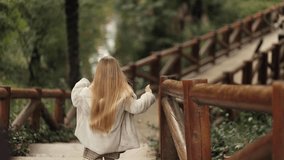 A cute blonde girl in stylish clothes, with beautiful hair, runs down the stairs in the park, atmospheric, dynamic video of a person in motion, beautiful colors and cinematic frame