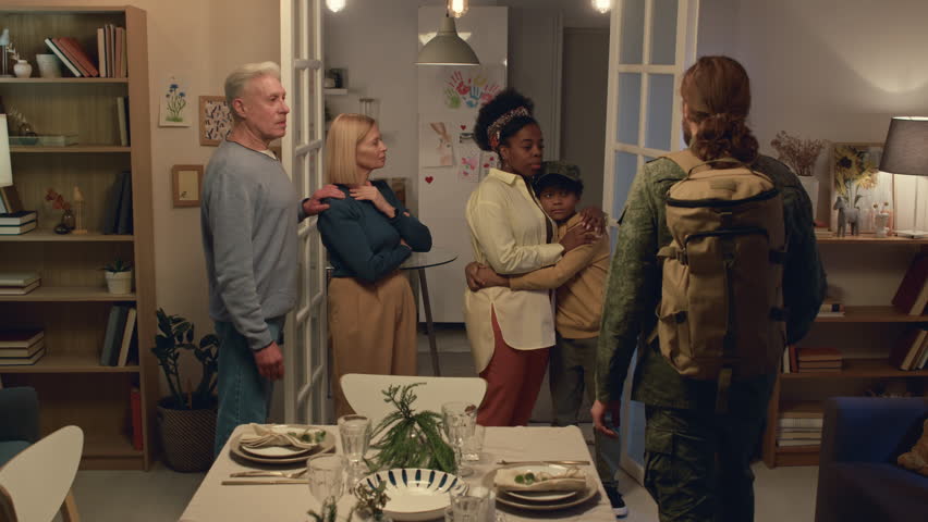 Medium long shot of intercultural family hugging man in uniform leaving for military service while standing in living room | Shutterstock HD Video #1111897131