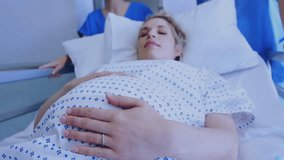 Fast moving clock over pregnant caucasian woman in bed moving in hospital corridor. Pregnancy, healthcare, expectancy, time, development, hospital and medical services digitally generated video.