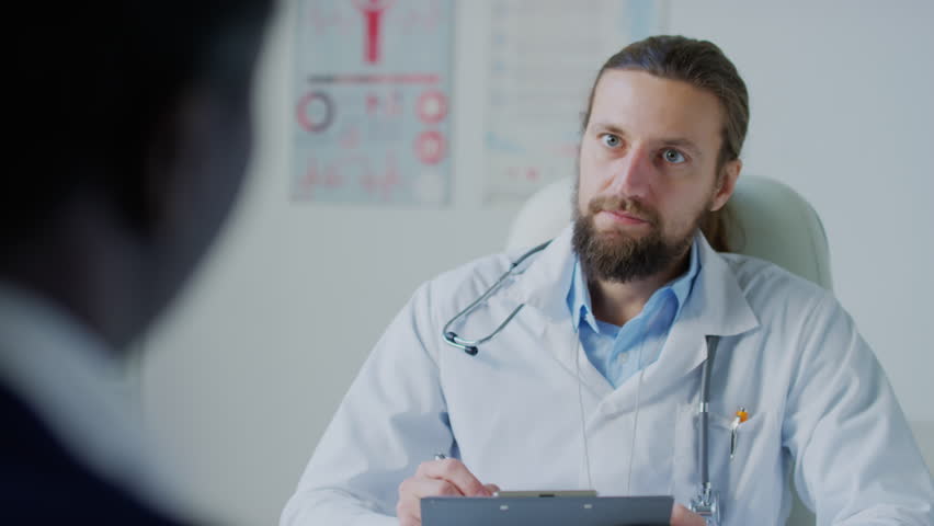 Medium over shoulder shot of male Caucasian practitioner writing down patients complaints in medical history in hospital | Shutterstock HD Video #1111897981