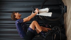 Professional cyclist sprinting out of saddle on stationary smart bicycle trainer. Man in cycling apparel hard pedaling on exercise bike, doing cardio workout. Indoor online fitness. Vertical video