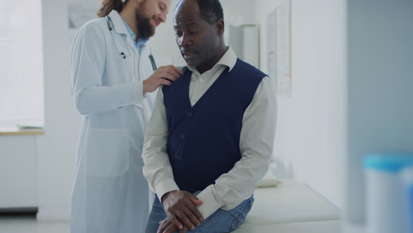 Medium tilt shot of smiling Caucasian physician doing checkup of African American patient who telling his complaints during appointment in private clinic | Shutterstock HD Video #1111900615