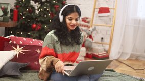 Beautiful young woman have video call conference meeting conversation on laptop sitting on bed near Christmas tree with decoration at cozy home Happy smiling lady talking by computer indoors