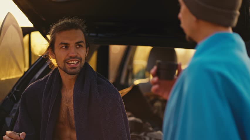 A brunette man in seven towels communicates with his friend who is drinking tea near a black car in the morning at Sunrise | Shutterstock HD Video #1111901597