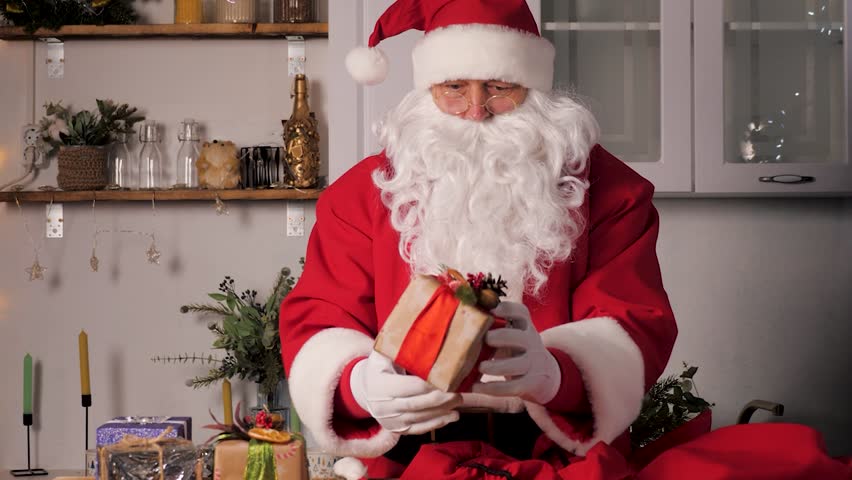 Old funny Santa Claus, puts gift boxes in a bag. Family favorite winter holiday. Christmas gifts from Santa. Merry Christmas. Santaclaus gift delivery. Festive New Year mood. Santa Claus brings gifts | Shutterstock HD Video #1111902115