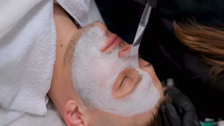 A beautician applies a moisturizing mask to a man's face. Man in cosmetic clinic, face close-up | Shutterstock HD Video #1111905243