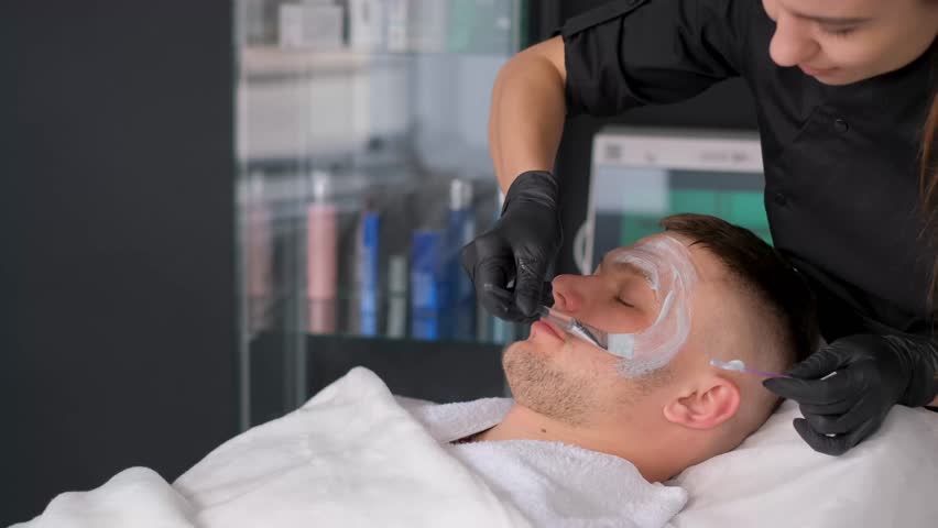 Male cosmetology. A cosmetologist, wearing gloves, applies a mask to a man's face. | Shutterstock HD Video #1111905251