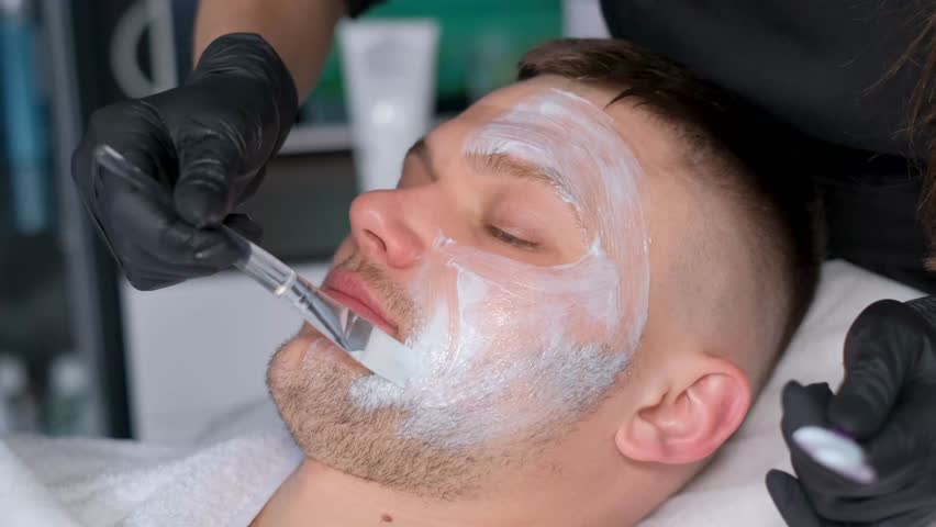 Cosmetologist is putting nutrition mask on the young man's face in the beauty salon. | Shutterstock HD Video #1111905265