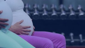 Fast moving clock over diverse pregnant women at gym massaging their bellies. Pregnancy, self care, expectancy, time, development, motherhood, prenatal and wellbeing digitally generated video.