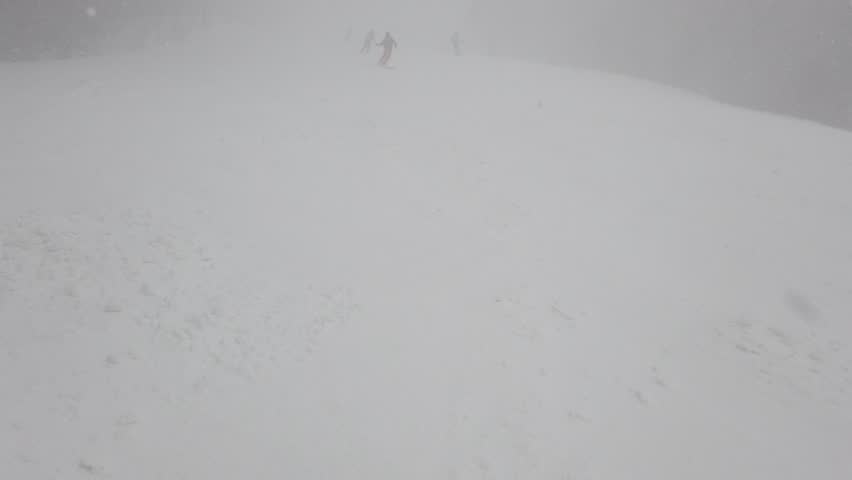 Blizzard of snow and wind on a ski slope. Skiers skiing in extreme conditions with fog and low visibility. Royalty-Free Stock Footage #1111905899