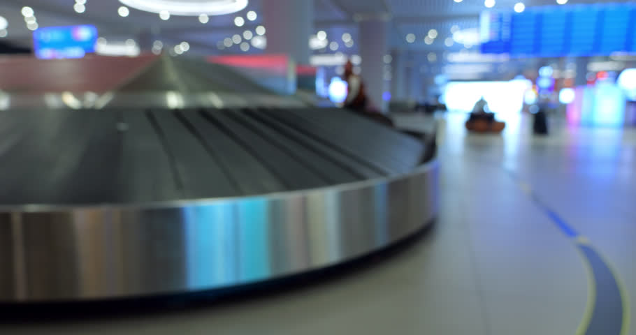 Baggage carousel turn corner, few suitcases move by, defocused view of luggage claim hall of modern international airport. Rather empty at early morning, silhouettes of few passengers visible on back | Shutterstock HD Video #1111906097