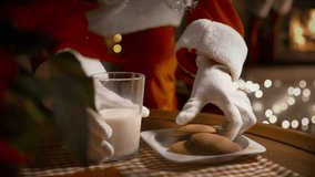 Santa Claus putting Christmas presents in socks over the fireplace, eating ginger cookies and drinking milk on Christmas night in the decorated living room with Christmas tree - Powered by Shutterstock - Get 15% off with code: PIKWIZARD15