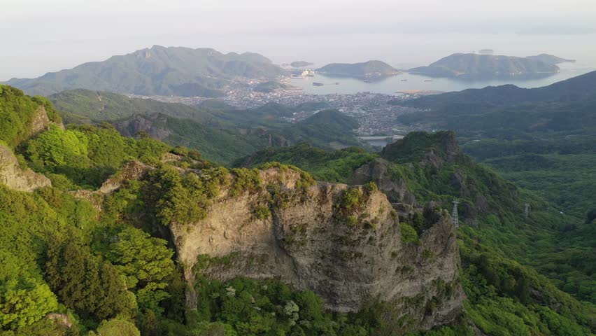 Aerial view from Takatori Viewpoint overlooking rugged cliffs and green forests of Kankakei Gorge on Shodoshima Island with a village on the coastline and islets in Seto Inland Sea, in Kagawa, Japan