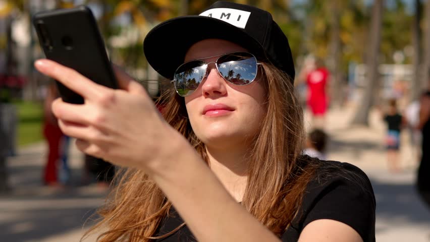 Young woman taking a selfie under palm trees at the beach - travel photography
